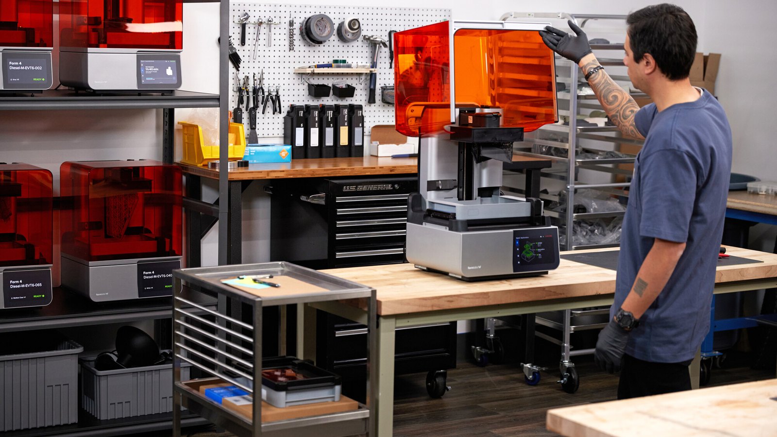 Técnico abriendo la tapa de una impresora 3D Formlabs Form 4 en un taller, con más unidades trabajando al fondo