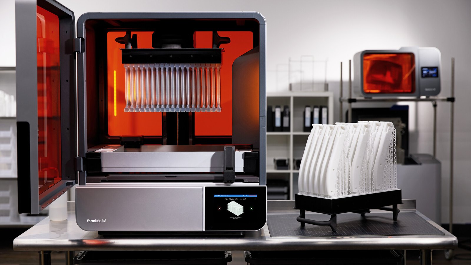 Impresora 3D de resina Formlabs Form 4B abierta junto a una bandeja con piezas médicas impresas