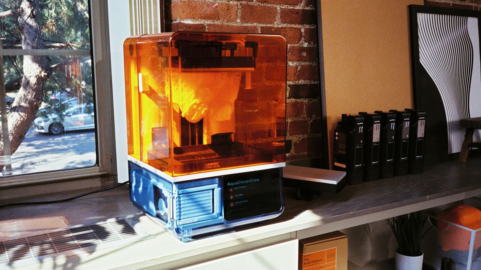 Impresora 3D Form Studio 1 de Formlabs imprimiendo junto a una ventana, con los cartuchos de resina Alpha alineados al lado